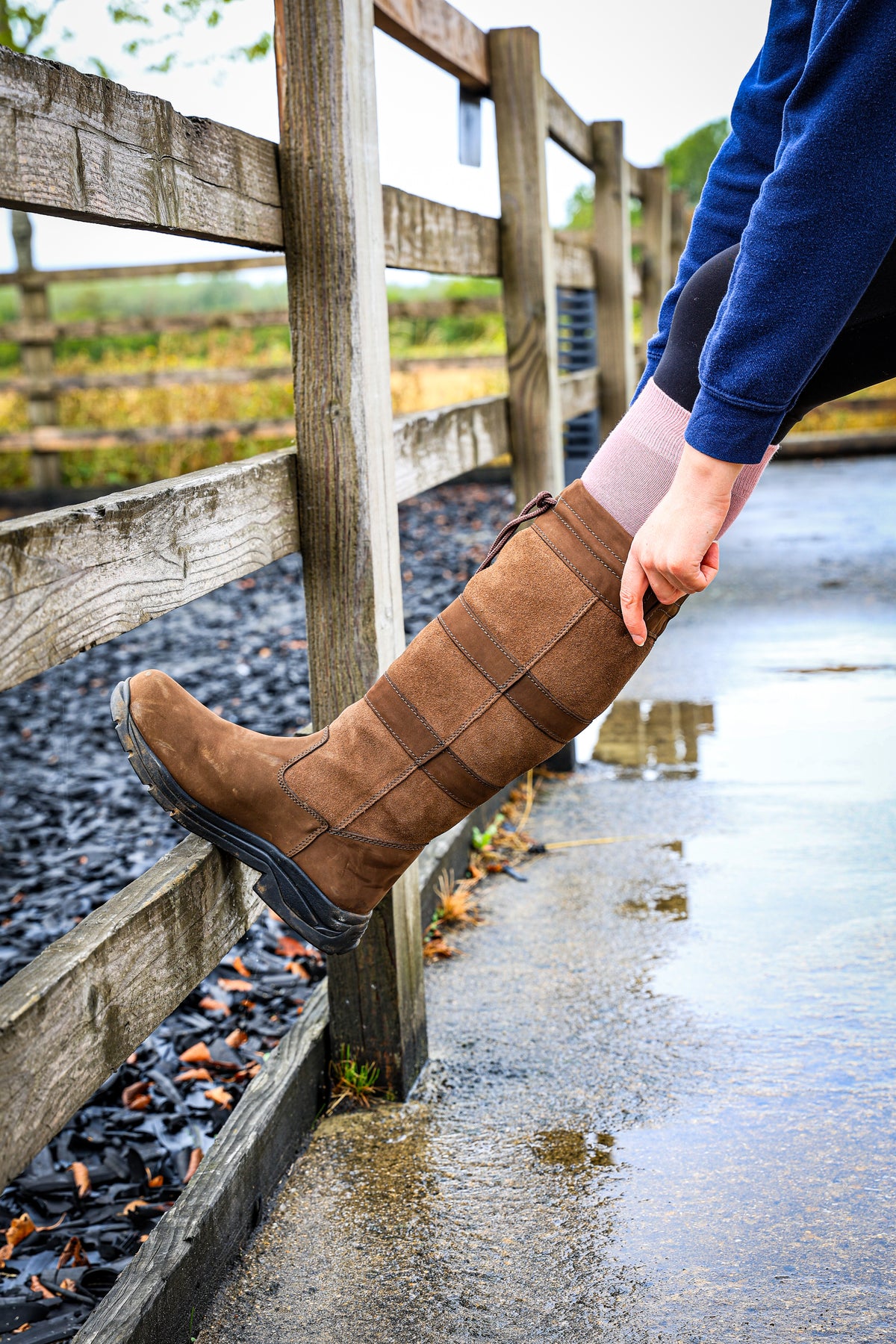 A woman wearing a brown pair of country boots pulling them over her Soleberie Pink Classic Long Socks.