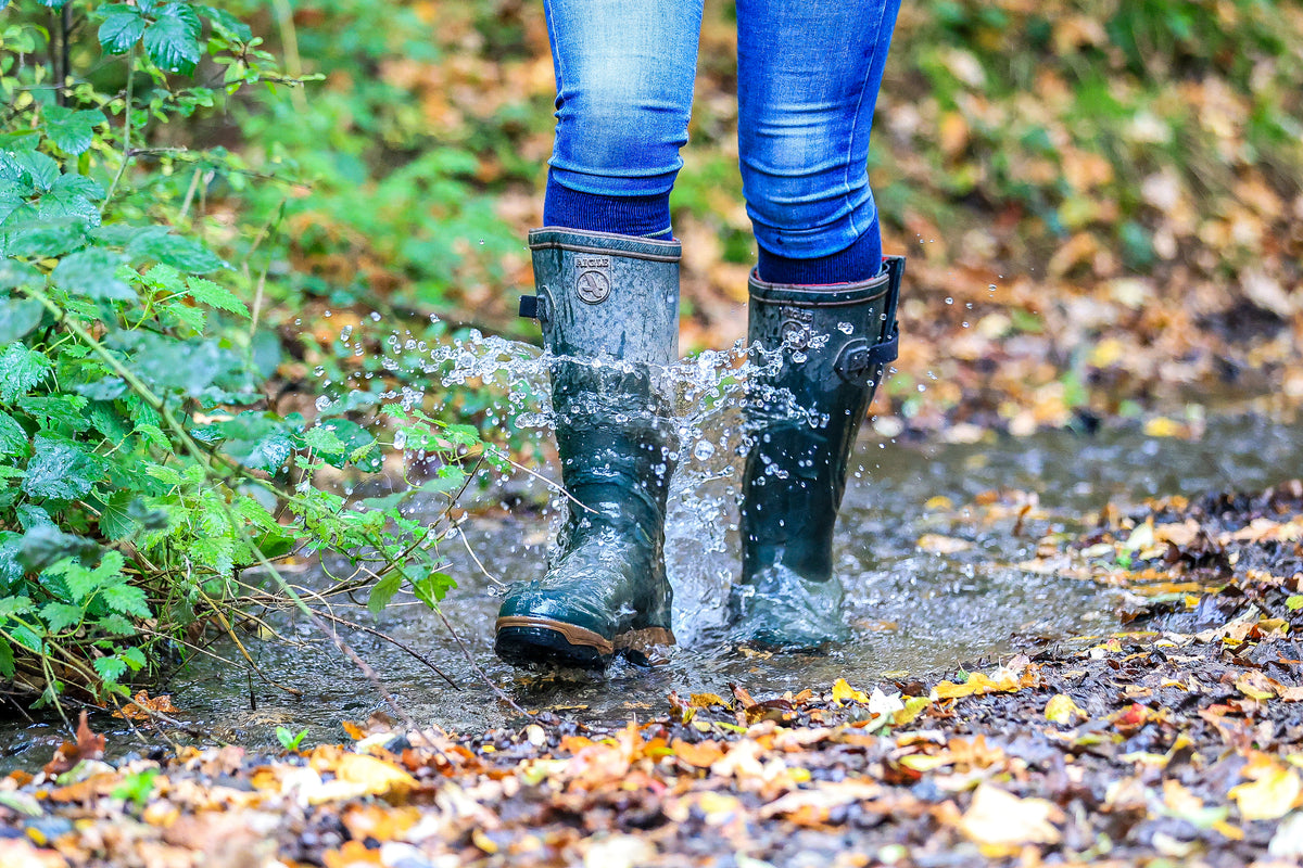 A woman wearing a pair of wellington boots and a pair of Navy Stripe Classic Long Socks from Soleberie. She is walking through a puddle in a wood. 